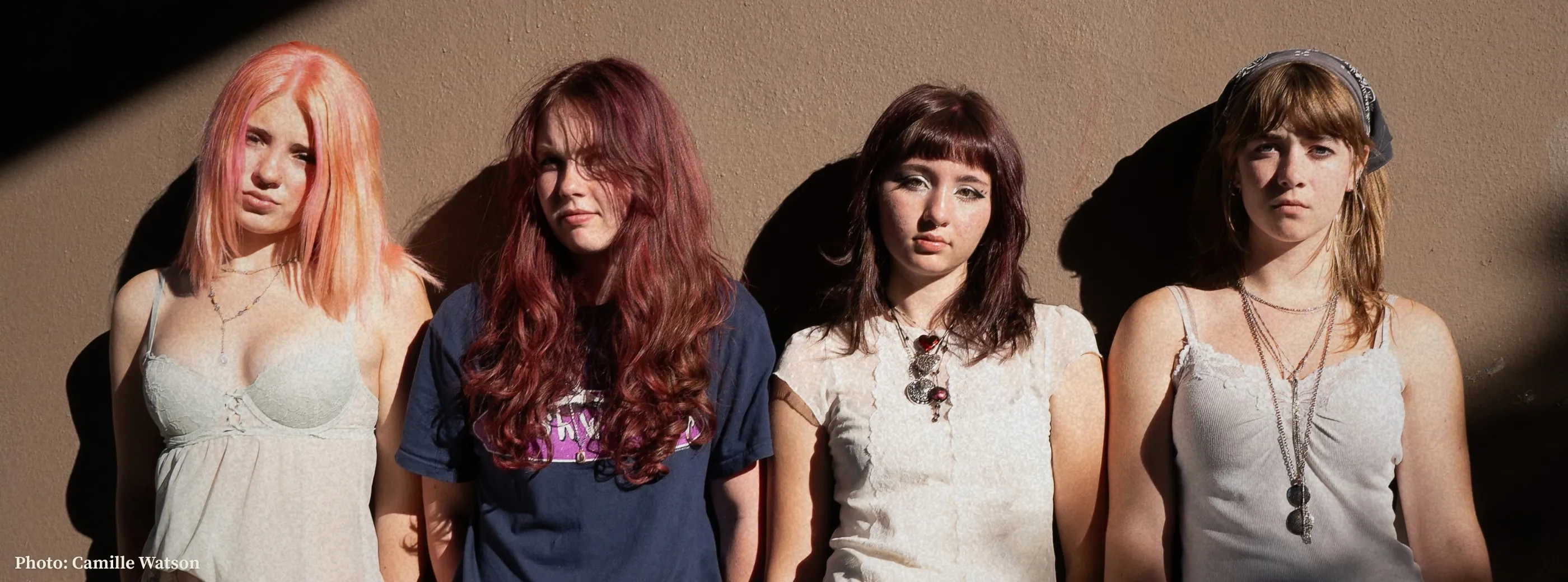 The four members of Chewing Gum standing against a sunlit tan wall.