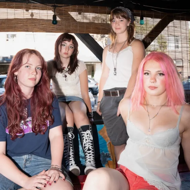 The four members of Chewing Gum sitting and standing together on a wooden porch.
