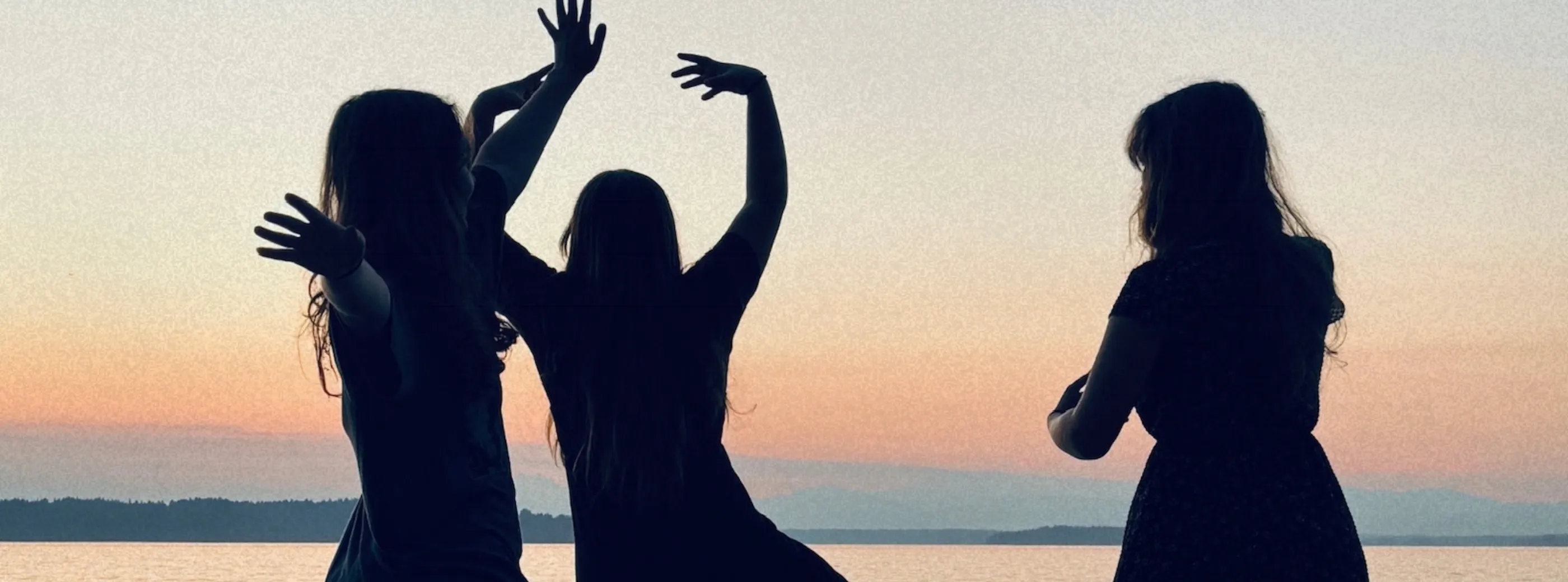 Silhouettes of the three members of Sad Dad Autumn dancing on a beach at sunset, arms raised.